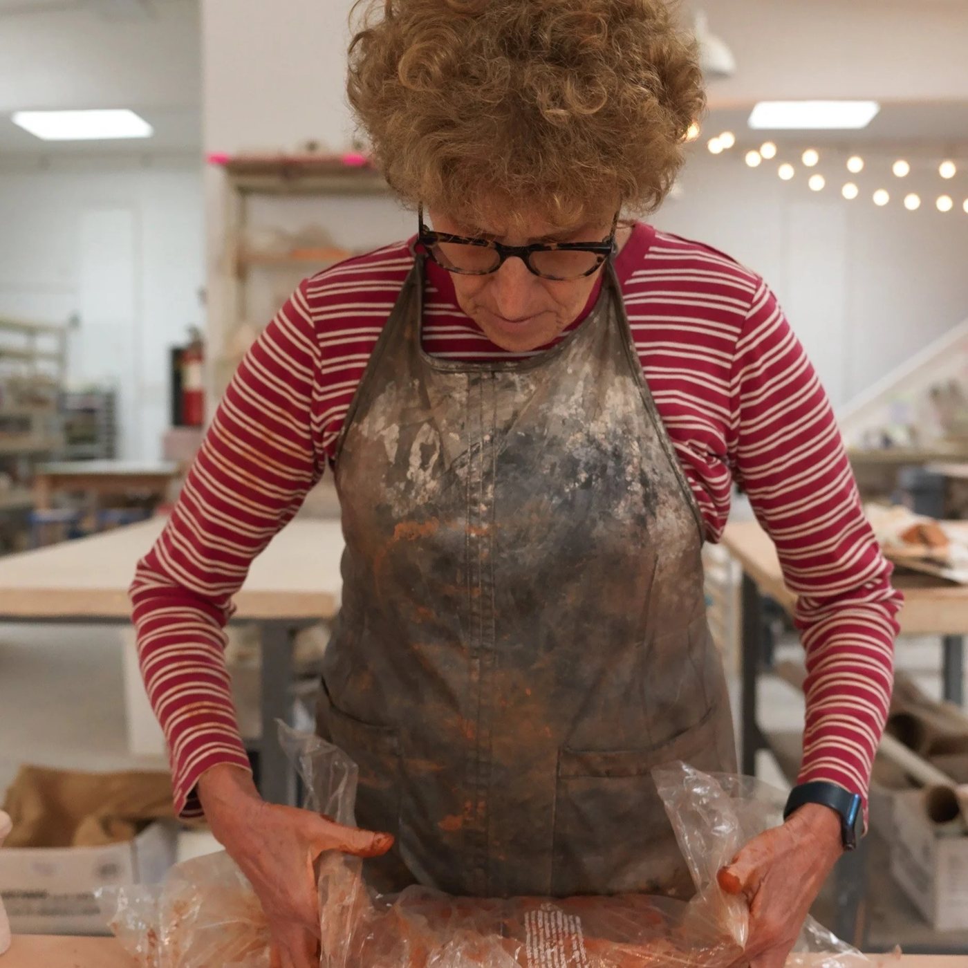 Pearl Jusem working clay at her studio bench, in a clay-dusted apron.
